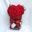 Heart-shaped bouquet of red roses in a clear cylinder vase, adorned with a red ribbon and tag.