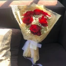 Bouquet of deep red roses with baby's breath, wrapped in textured beige paper and tied with a white ribbon.