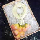 Gift box with a white jasmine garland and a bouquet of yellow and pink flowers.