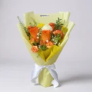 Zesty Bloom bouquet with orange roses, carnations, and yellow filler flowers, wrapped in light yellow paper with a white ribbon.