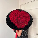 99 red roses arranged in a heart shape, a large bouquet with black wrapping and a red bow.