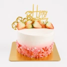 Pink ombre Tres Leches cake topped with strawberries and a gold "Happy Birthday" topper, on a gold cake board.