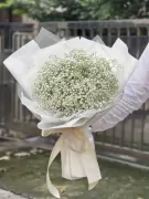 A bouquet of white baby's breath wrapped in white paper and tied with a cream ribbon.