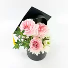 Pink roses and white mums in a black graduation hat box with a yellow tassel.