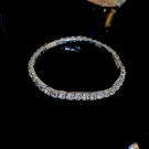 A silver tennis bracelet with many clear stones on a black background.