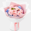 A bouquet of pink roses and blue hydrangeas wrapped in pink and white paper, tied with a pink ribbon.