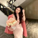 Woman in pink dress and blazer holds a round box of peach and cream roses.