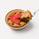 A fork lifts a slice of molten chocolate chip cookie pie, revealing a gooey Nutella center and red heart.