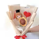 Crocheted girl graduate with sunflower and heart in a bouquet with brown paper wrapping.