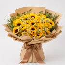 Bouquet of bright yellow sunflowers with green foliage, wrapped in brown paper and tied with twine.