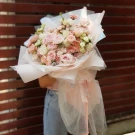 A giant bouquet of pink roses and white blooms, wrapped in sheer pink and white paper.