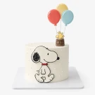 Snoopy and Woodstock float in balloons above a white cake with Snoopy on the side.