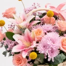 Pink lilies and peach roses in a woven basket, with delicate pink filler flowers and eucalyptus.
