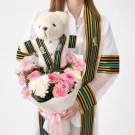 A graduation bear wearing a Chulalongkorn University gown holds a pastel flower bouquet tied with a pink ribbon.