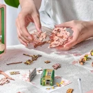 Hands assemble a wooden 3D sakura tree puzzle next to a miniature green tram and vintage radio.