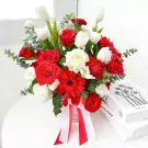 A floral arrangement in a white box with red and white roses, tulips, gerberas, carnations, lisianthus, and eucalyptus.