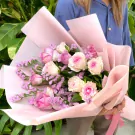 Pink and purple roses with statice in a pink wrapper, held by a person.