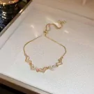 Gold bracelet with five adjustable heart charms, some adorned with clear stones.