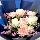Bouquet of white and pink roses with small pink dried flowers, wrapped in dark blue paper.