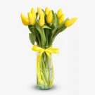 Yellow tulips arranged in a clear glass vase with a yellow ribbon tied around it.