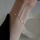 Gold-tone bracelet with three small heart charms on a delicate chain worn on a wrist.