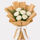 A bouquet of white roses with greenery wrapped in brown paper and tied with a white ribbon.