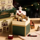 Christmas chocolate box filled with gold-wrapped chocolates, with luxury manor-themed boxes in background.