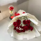 Red roses in a bouquet and a single rose under glass with fairy lights.