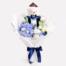 Graduation bouquet with teddy bear in academic regalia and blue and white flowers.