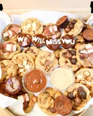 Cookies and brownies with "We Will Miss You" frosting, dips, and sprinkles in a box.