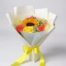 Bouquet of a sunflower, yellow rose, coral carnations, and small white flowers wrapped in white paper, tied with a yellow ribbon.