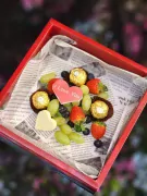 Red box filled with chocolates, strawberries, grapes, and a white chocolate heart.