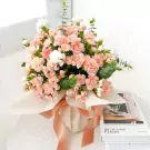 Pink carnation and white flower bouquet in a vase, tied with a ribbon, next to a book.