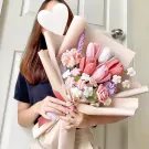 Crocheted pink tulips and carnations in a bouquet with green leaves, held by a person.
