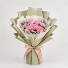 Pink carnations and dusty miller in a green bouquet tied with a peach ribbon.