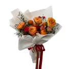 Orange roses, carnations, eucalyptus, and tangerines in a white paper bouquet with red ribbon.