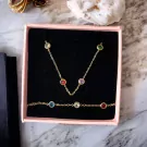Gold necklace and bracelet set with multi-colored gemstones in a pink box.