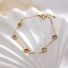Gold chain bracelet with colorful gemstones, including purple, green, red, blue, and teal, on a white, wavy surface.