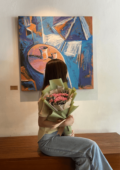 Person holding pink carnation and dusty miller bouquet in front of abstract painting.