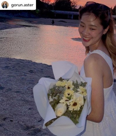 Woman in white dress holding white roses and gerberas bouquet at sunset.
