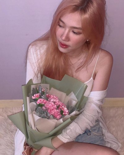Woman holding a bouquet of pink carnations and dusty miller, wrapped in green paper.