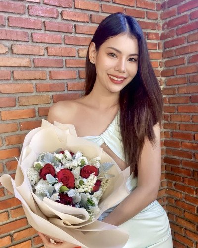 Woman in a light green dress holds a bouquet of red roses, white statice, and dusty miller.