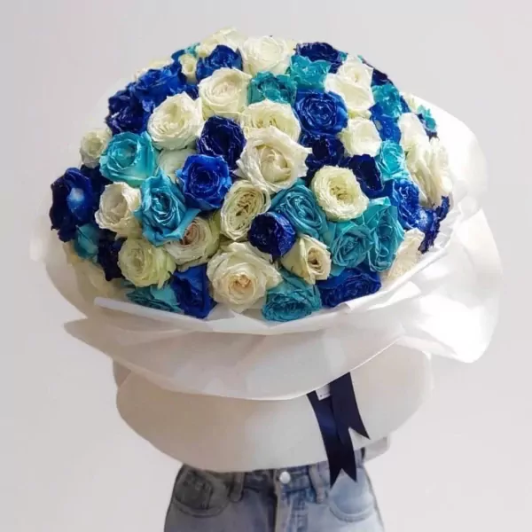 Large bouquet of blue, turquoise, and white roses wrapped in white paper with a dark blue ribbon.