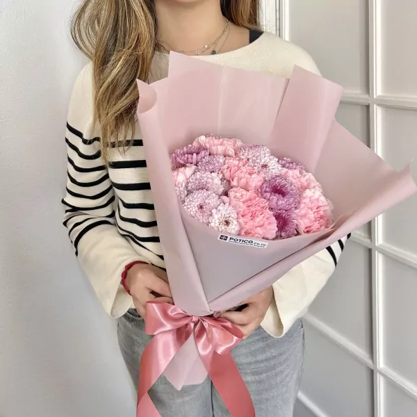 Woman holding a pink bouquet with carnations and purple and pink mums, tied with a pink ribbon.