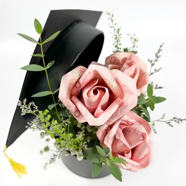 Black graduation cap with money roses and greenery in a grey vase.