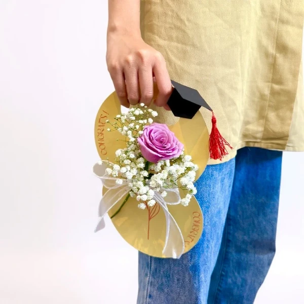 Graduation gift of a single purple rose and baby's breath with a graduation cap decoration.