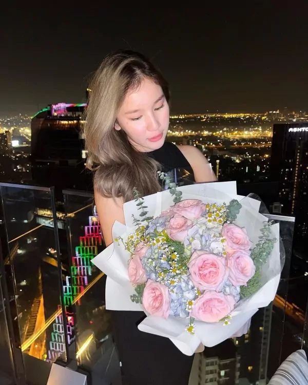 Woman holding a bouquet of pink roses, blue hydrangeas, and daisies at night.