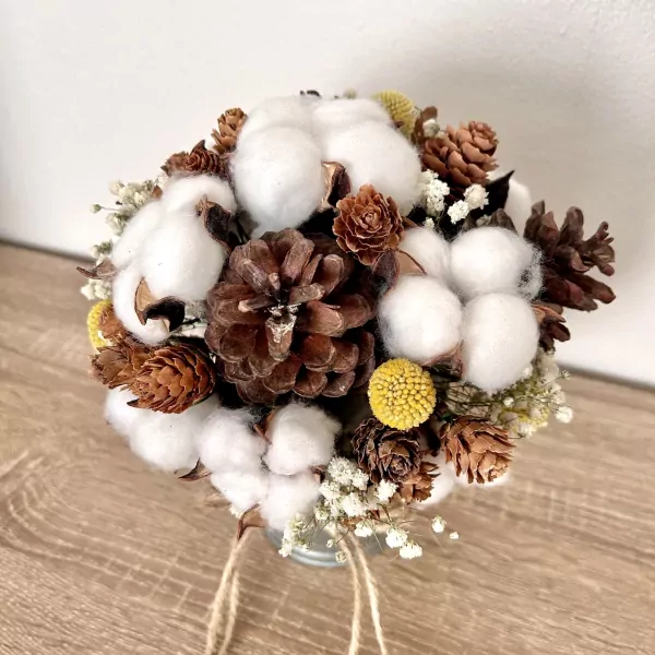 Round bouquet of cotton flowers, pine cones, and small yellow flowers in a metal pot.