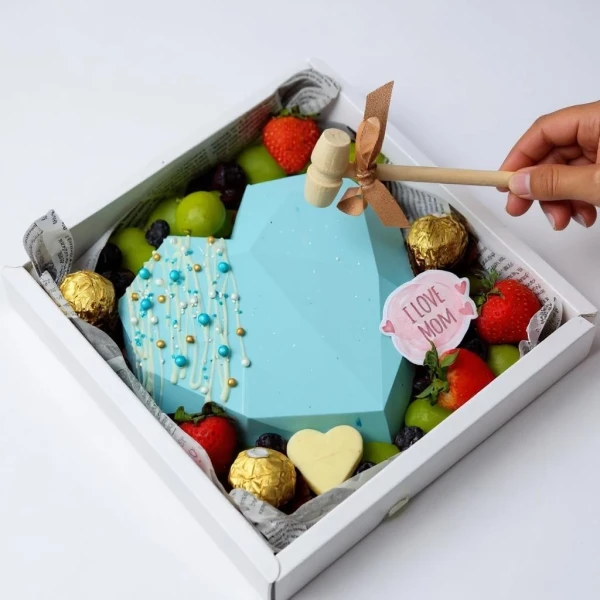Blue geometric heart-shaped chocolate cake with fruits, chocolates, and a small hammer.