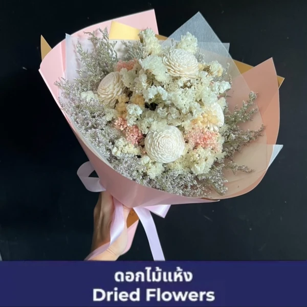 A bouquet of dried flowers in pastel colors, wrapped in pink paper and tied with a ribbon.